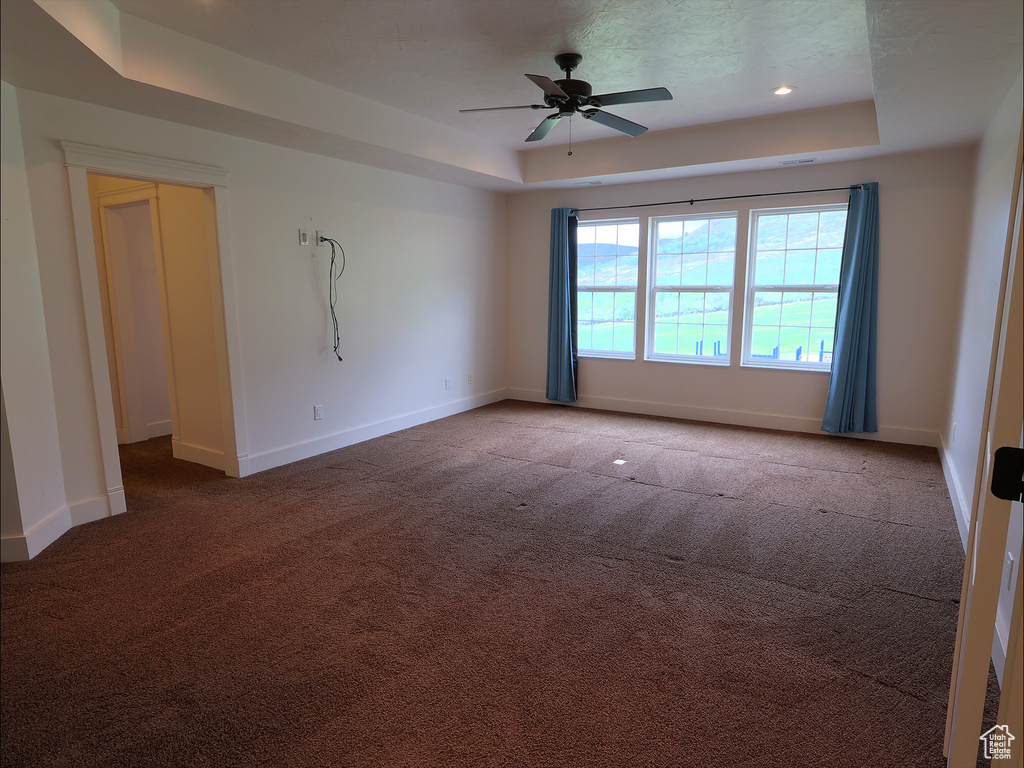 Carpeted empty room with a raised ceiling, ceiling fan, baseboards, and recessed lighting