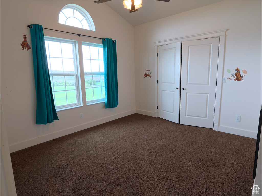 Unfurnished bedroom with dark carpet, lofted ceiling, baseboards, a closet, and a ceiling fan