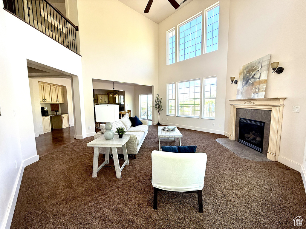 Living room featuring dark colored carpet, ceiling fan, a fireplace with flush hearth, and a high ceiling
