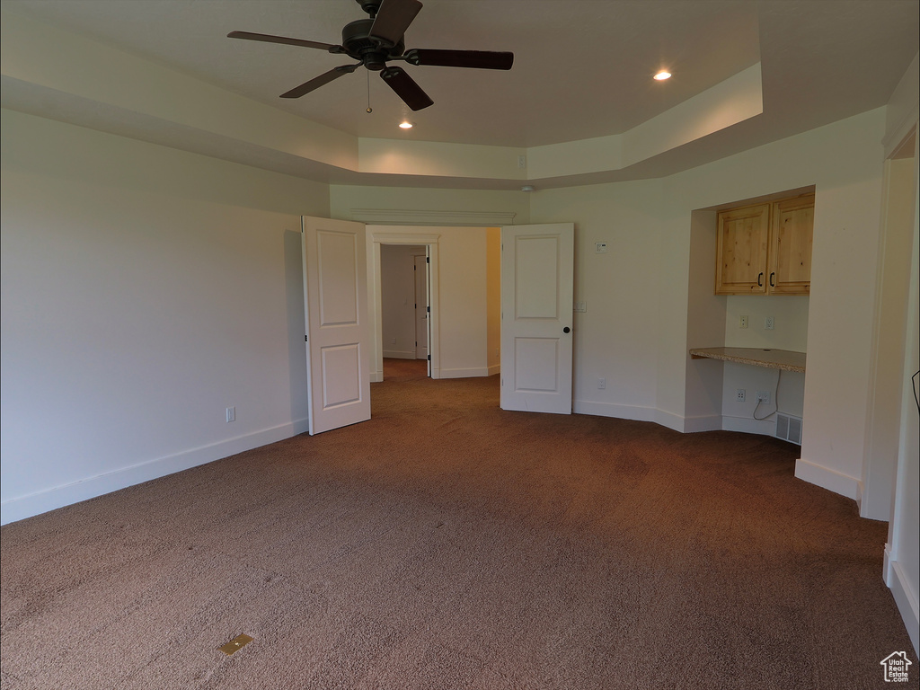 Unfurnished bedroom featuring dark carpet, a tray ceiling, baseboards, recessed lighting, and ceiling fan