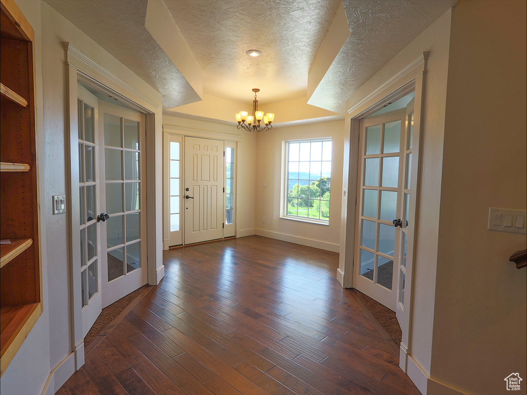 Foyer entrance with french doors, a chandelier, a textured ceiling, dark wood finished floors, and baseboards