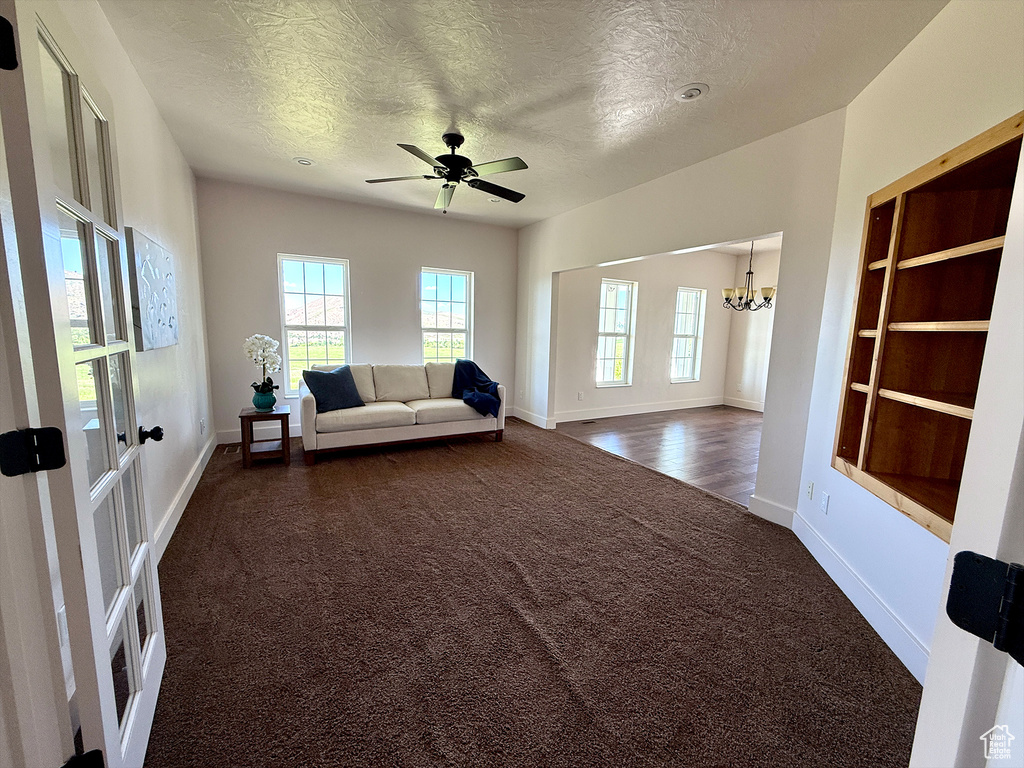 Living area with dark carpet, a textured ceiling, plenty of natural light, a chandelier, and ceiling fan