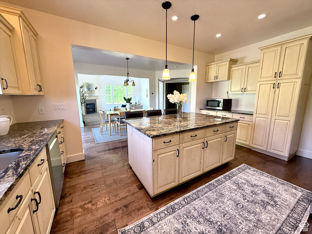 Kitchen featuring stainless steel appliances, cream cabinetry, dark wood-style floors, recessed lighting, and dark stone counters