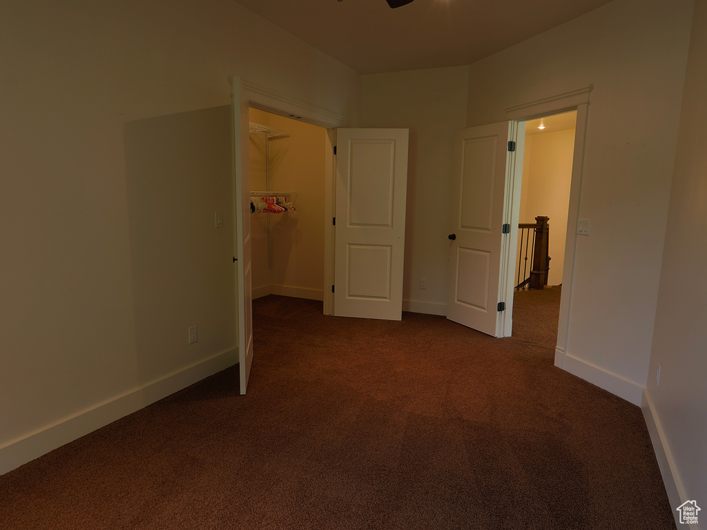 Unfurnished bedroom with dark carpet, a spacious closet, and baseboards