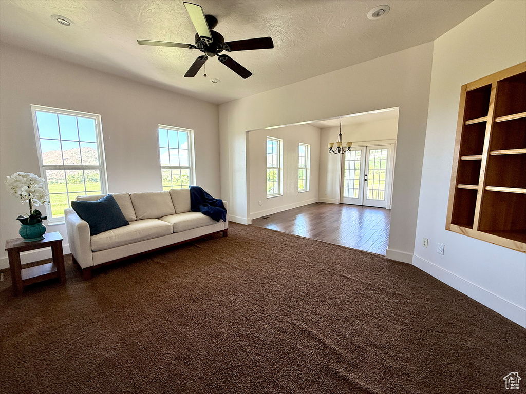 Living room featuring dark colored carpet, a chandelier, a ceiling fan, french doors, and a textured ceiling