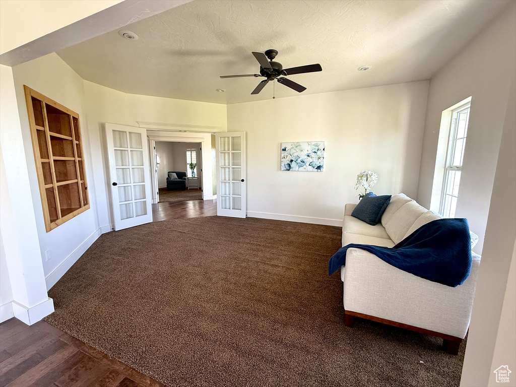 Living area featuring french doors, ceiling fan, built in shelves, dark colored carpet, and dark wood finished floors
