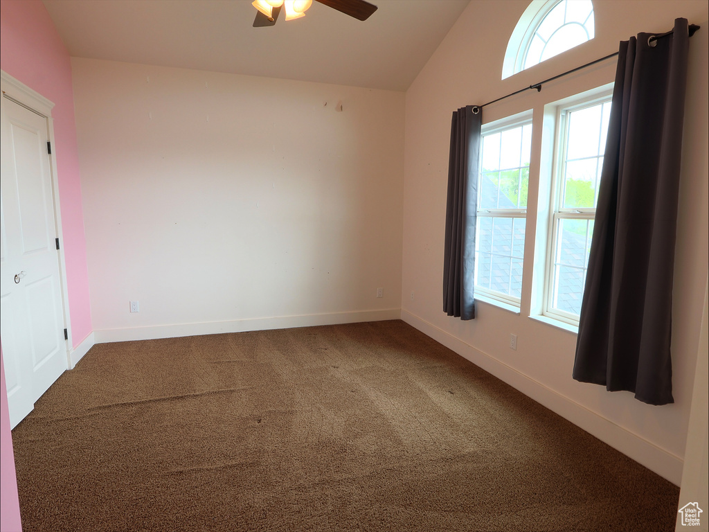 Carpeted empty room featuring lofted ceiling, ceiling fan, and baseboards