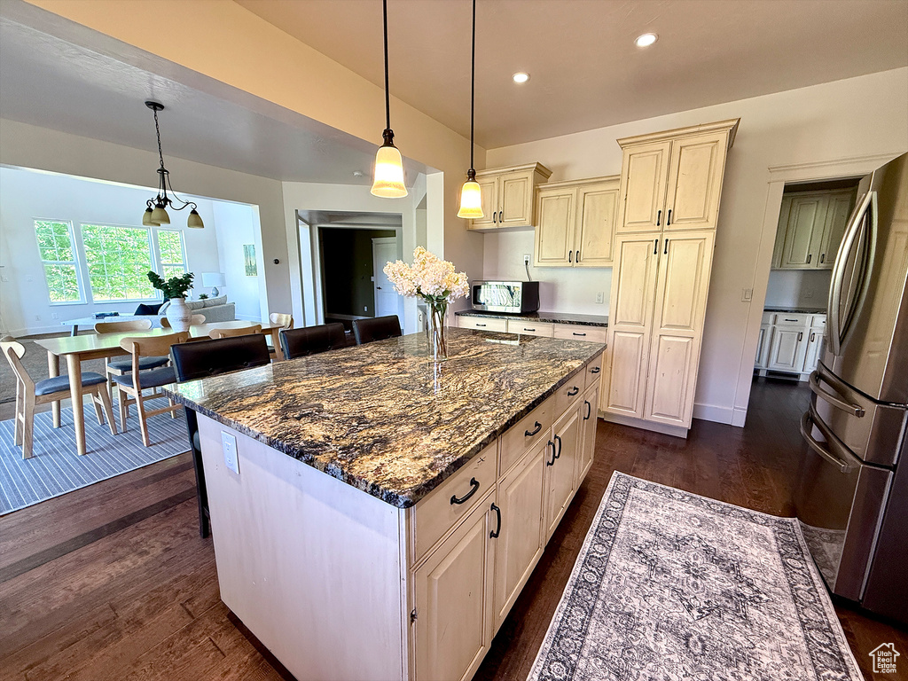 Kitchen with appliances with stainless steel finishes, cream cabinetry, dark wood-style flooring, dark stone countertops, and decorative light fixtures