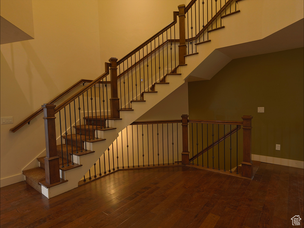 Stairs with wood-type flooring, a towering ceiling, and baseboards