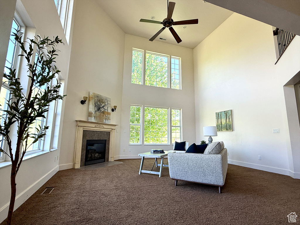Living area featuring a towering ceiling, dark carpet, a tile fireplace, and a ceiling fan