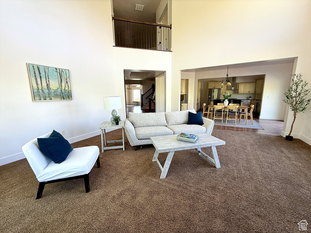 Living area with a high ceiling, dark carpet, and stairs