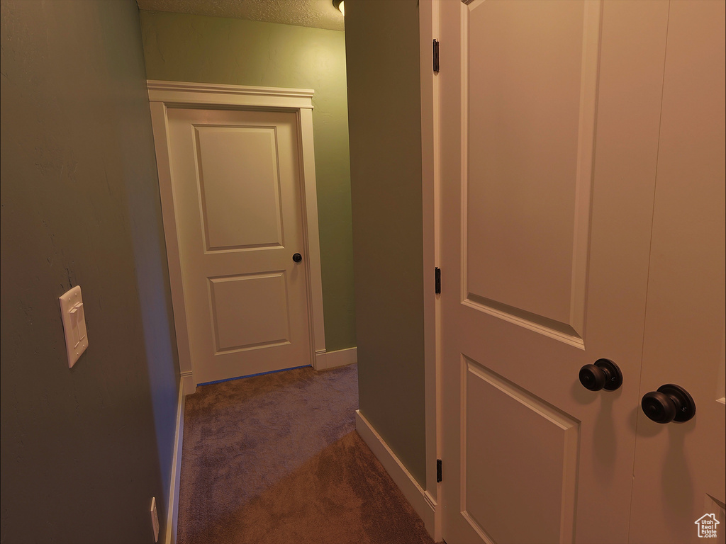 Hall featuring dark colored carpet and baseboards