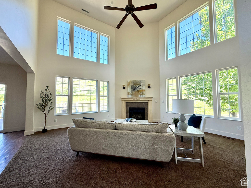 Living room featuring a high ceiling, ceiling fan, a fireplace, and dark colored carpet
