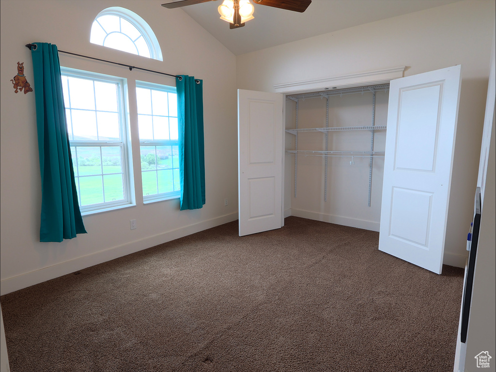 Unfurnished bedroom with dark colored carpet, multiple windows, vaulted ceiling, and a closet