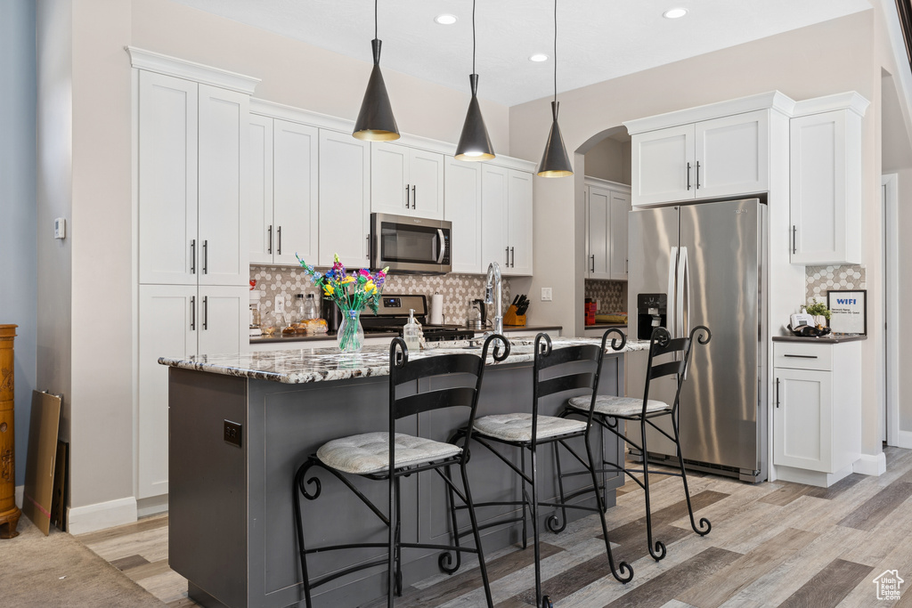 Kitchen with stainless steel appliances, light wood-style flooring, decorative backsplash, arched walkways, and recessed lighting