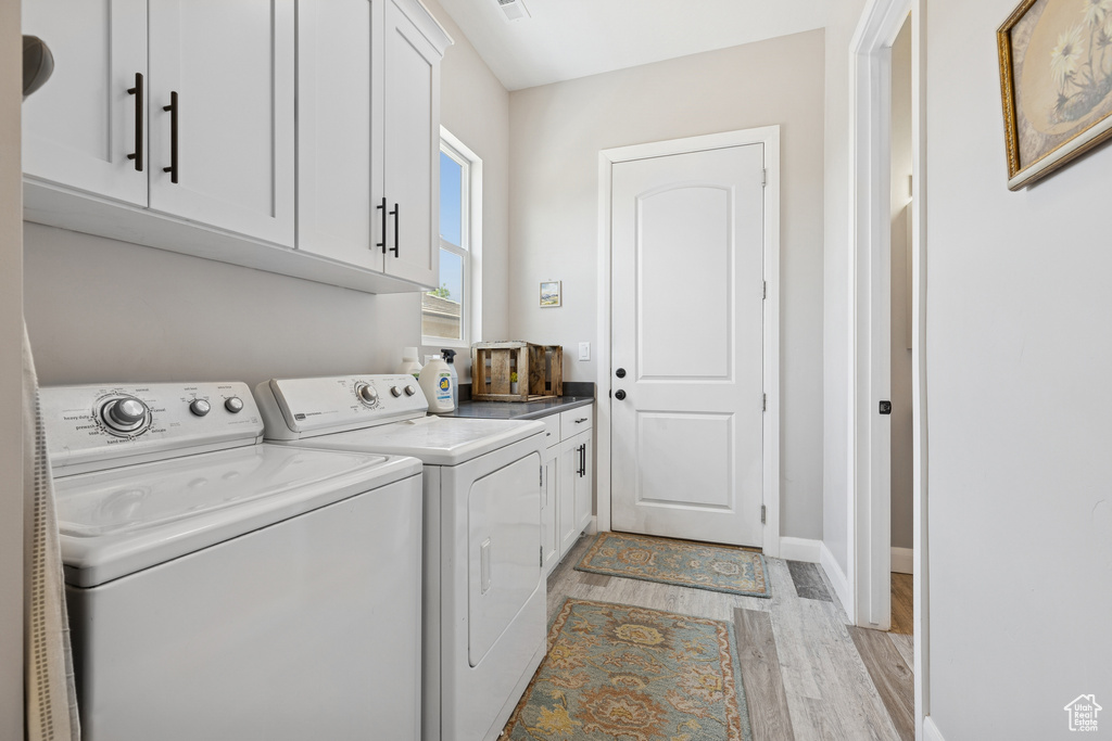 Washroom with washing machine and dryer, cabinet space, light wood-type flooring, and baseboards