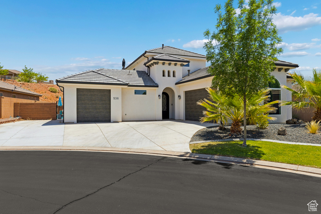 View of front facade featuring a garage, concrete driveway, stucco siding, and a tile roof