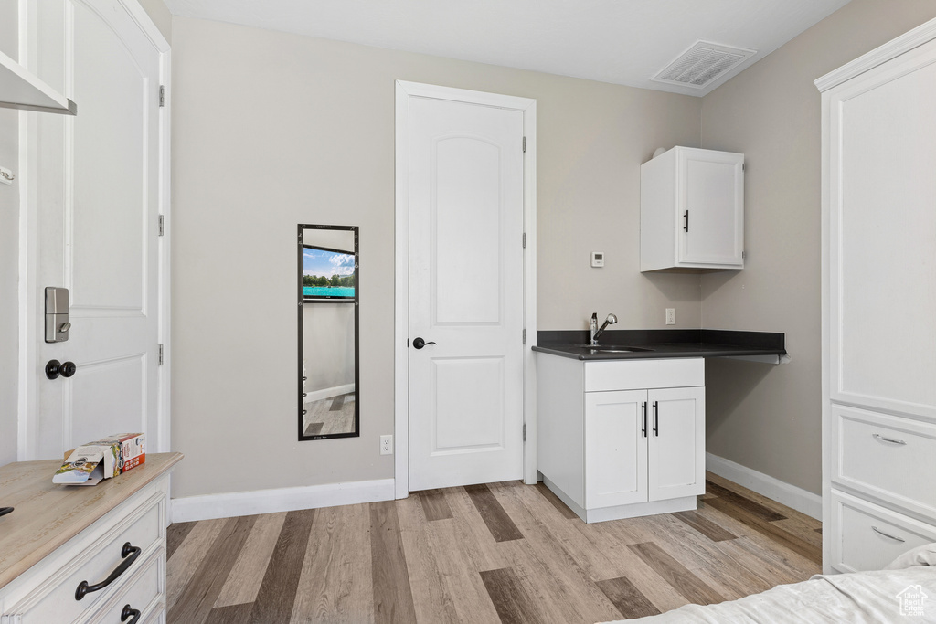 Kitchen featuring light wood-type flooring, white cabinetry, a sink, and baseboards