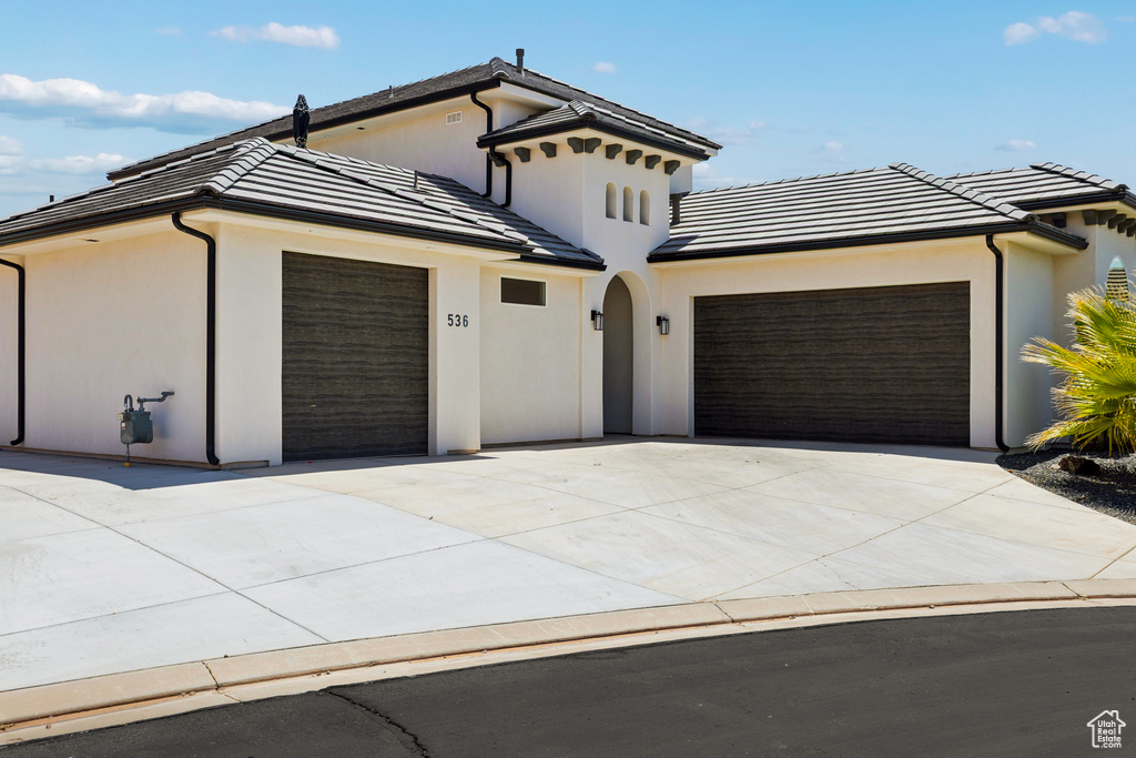 View of front of property with an attached garage, concrete driveway, a tiled roof, and stucco siding