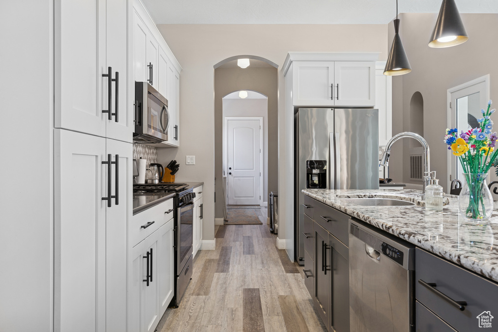 Kitchen featuring appliances with stainless steel finishes, light wood-type flooring, a sink, and white cabinetry