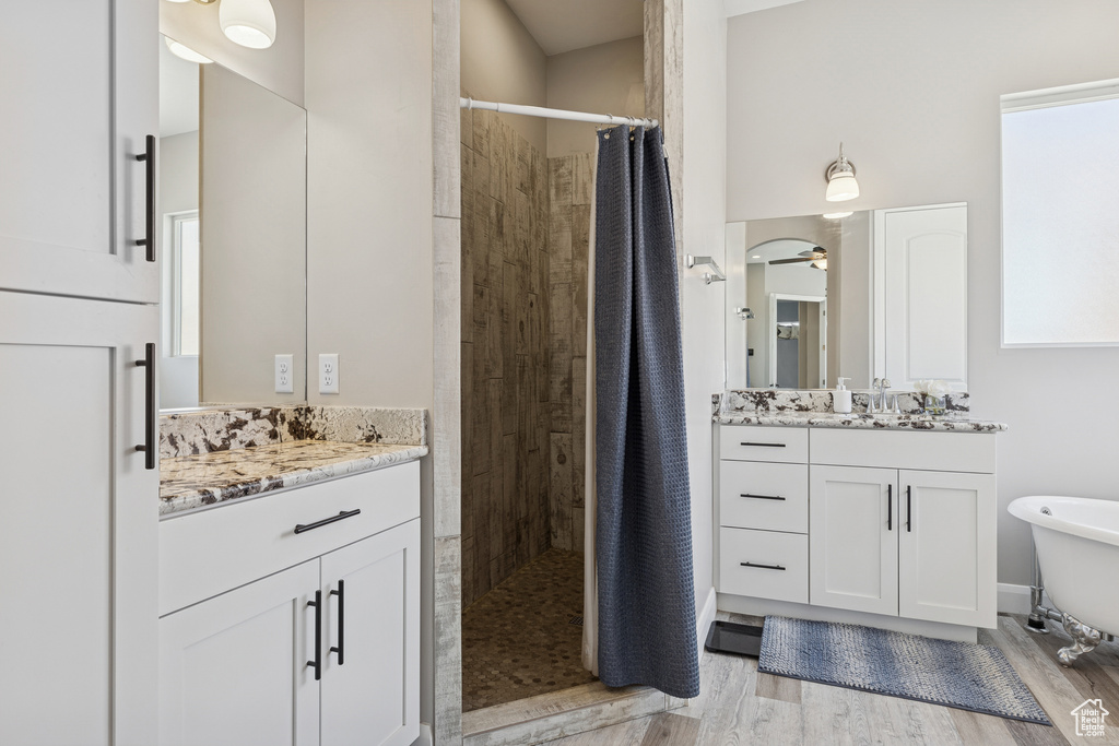 Full bath with a tile shower, two vanities, wood finished floors, and a freestanding bath