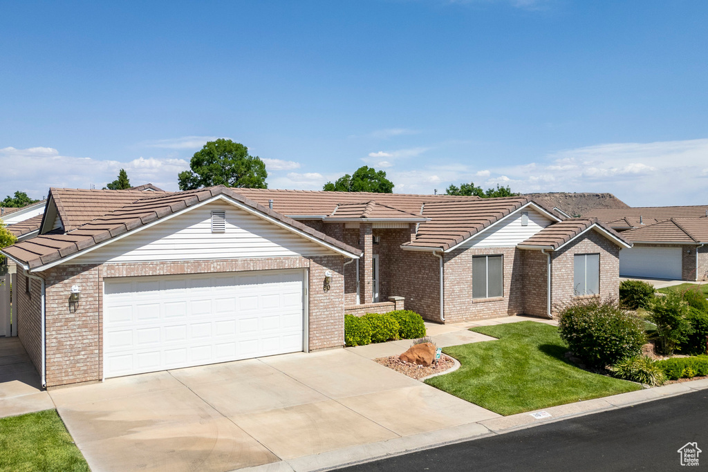 View of front of home featuring a tiled roof, a front yard, an attached garage, brick siding, and driveway
