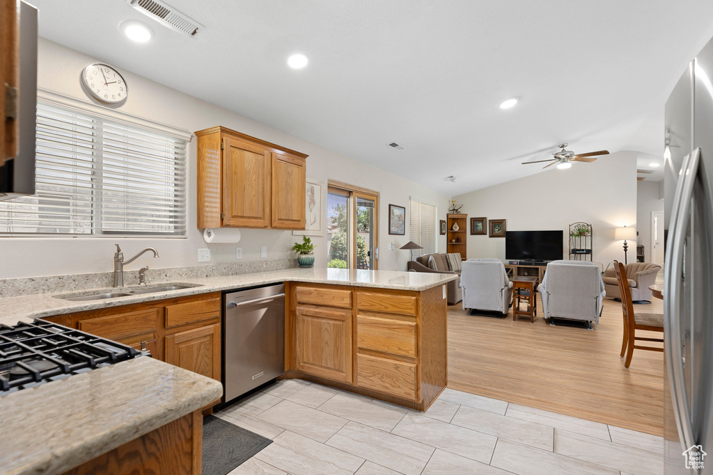 Kitchen featuring appliances with stainless steel finishes, a peninsula, a sink, open floor plan, and vaulted ceiling