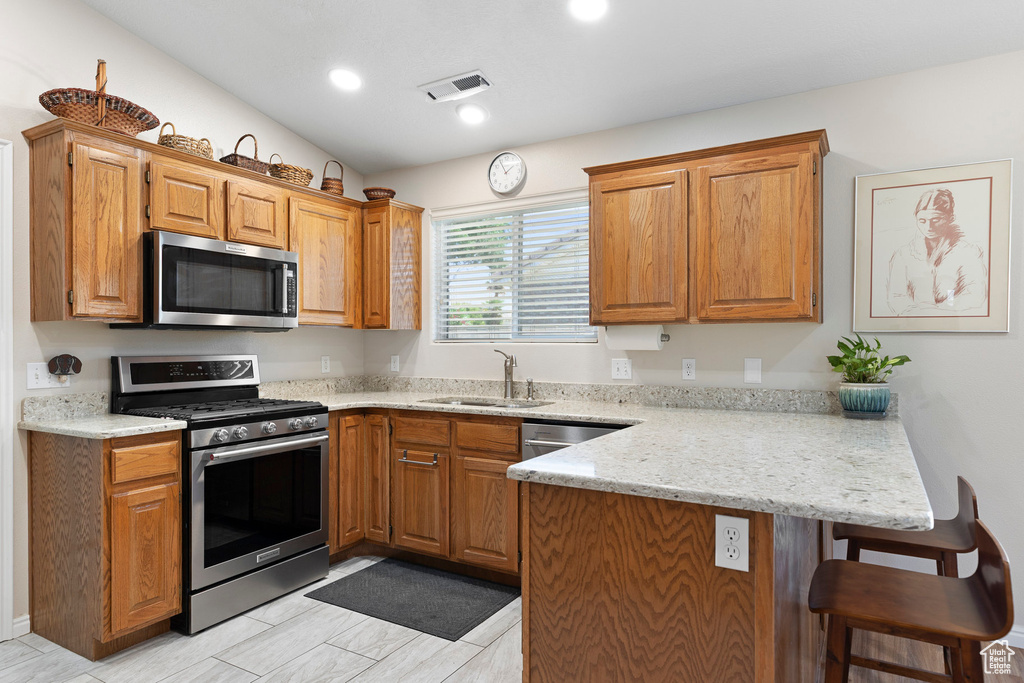 Kitchen featuring appliances with stainless steel finishes, a peninsula, a kitchen breakfast bar, a sink, and brown cabinetry