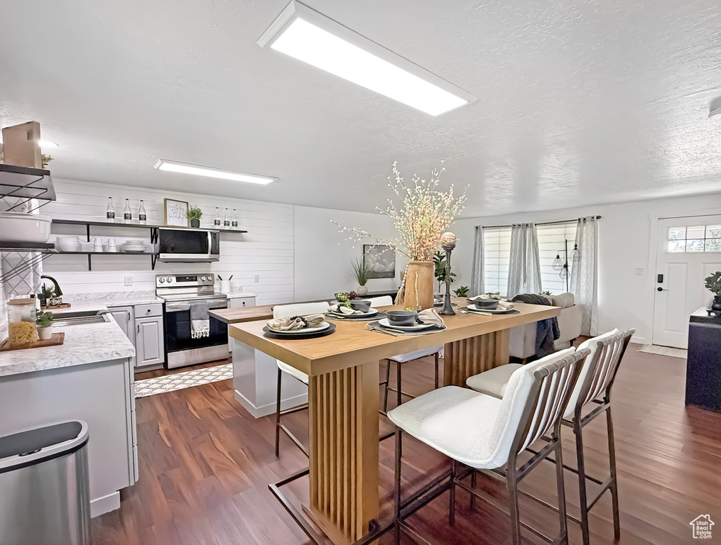 Kitchen with stainless steel appliances, a sink, open shelves, dark wood-type flooring, and a breakfast bar area
