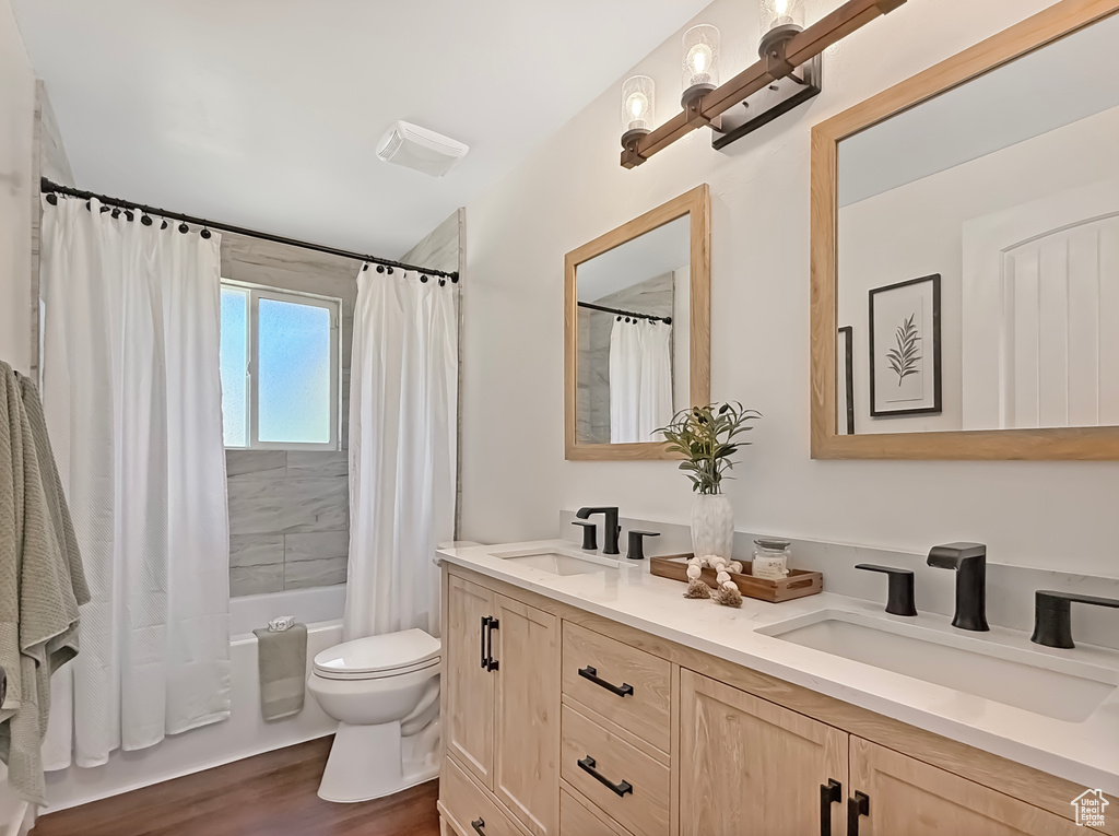 Bathroom featuring double vanity, shower / tub combo with curtain, toilet, and wood finished floors