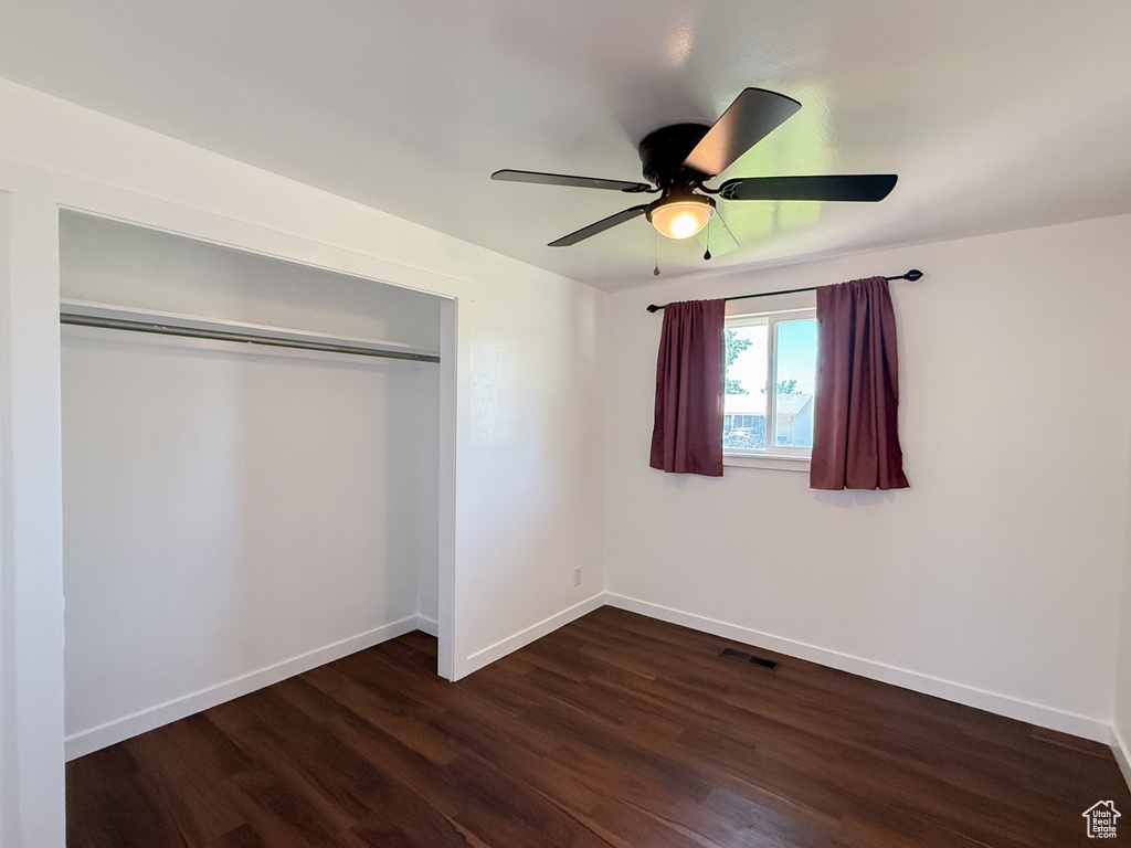 Unfurnished bedroom featuring dark wood-type flooring, baseboards, a closet, and a ceiling fan