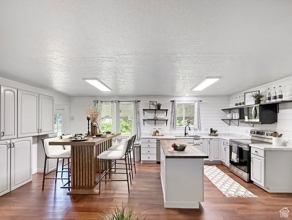 Kitchen with stainless steel electric stove, a center island, open shelves, plenty of natural light, and a textured ceiling