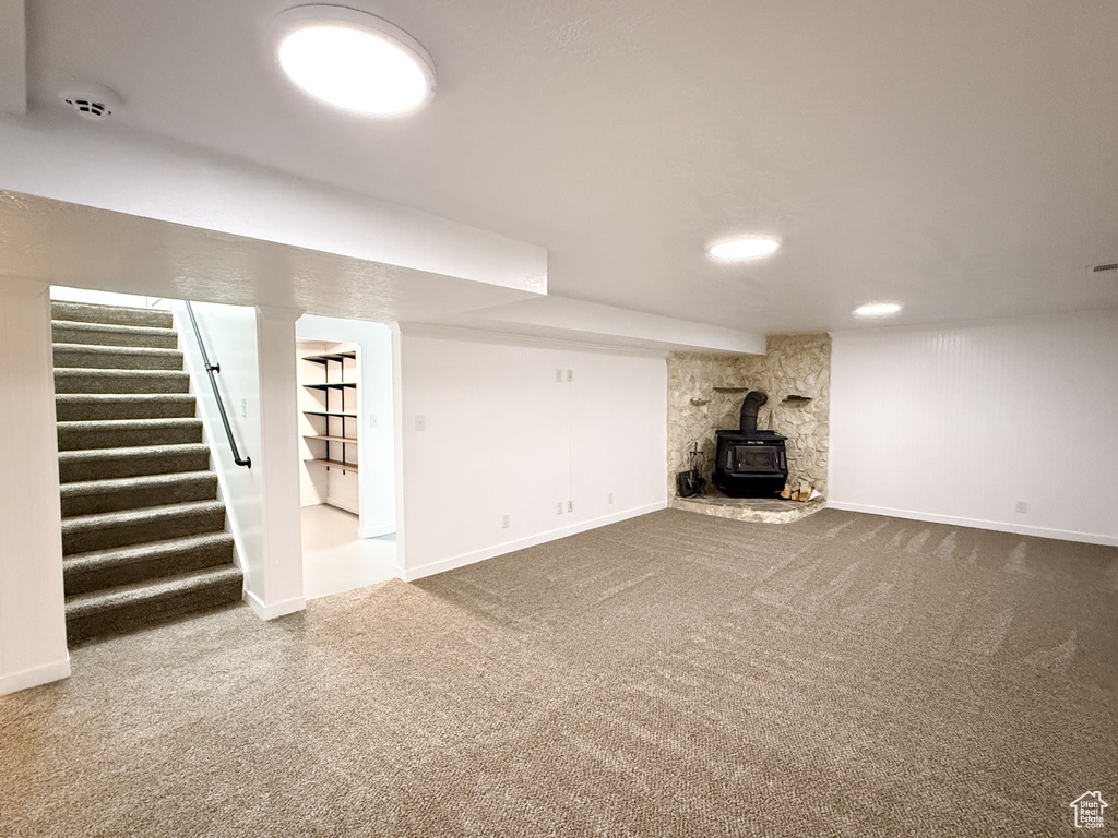 Unfurnished living room featuring carpet, a wood stove, stairway, and baseboards
