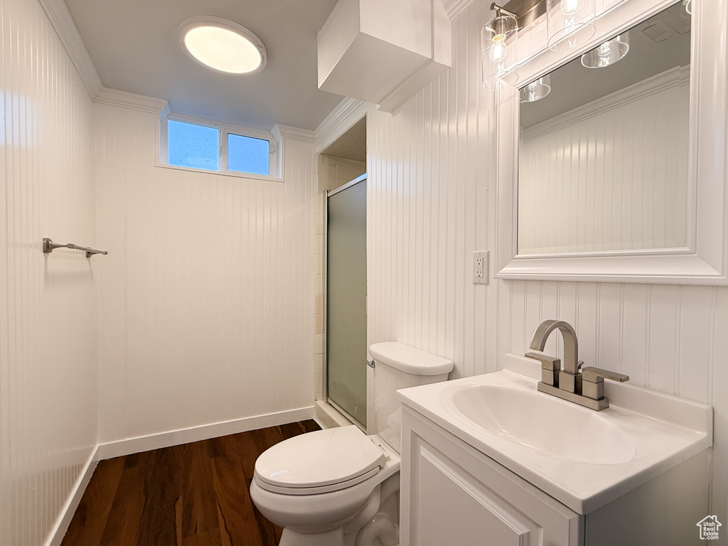 Bathroom featuring a shower with door, wood finished floors, toilet, vanity, and ornamental molding