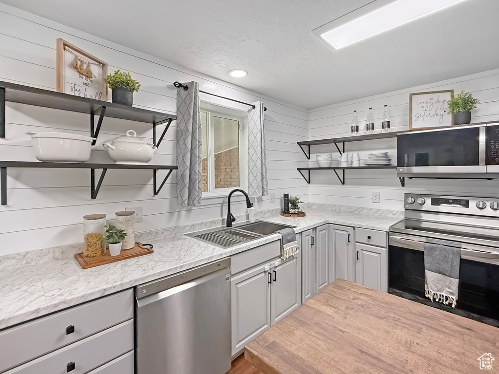 Kitchen with open shelves, appliances with stainless steel finishes, a sink, gray cabinetry, and a textured ceiling