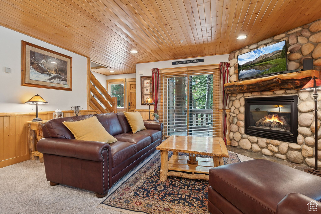 Living area featuring wood ceiling, wainscoting, a stone fireplace, stairs, and light carpet