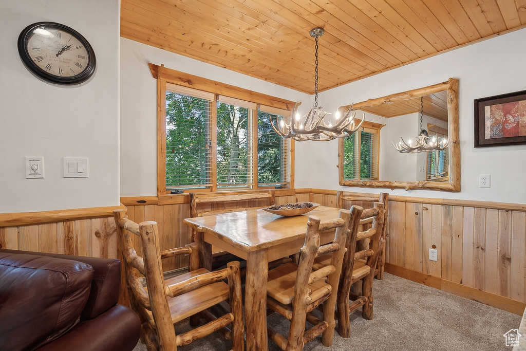 Dining room featuring a wainscoted wall, a chandelier, wooden ceiling, wood walls, and light colored carpet