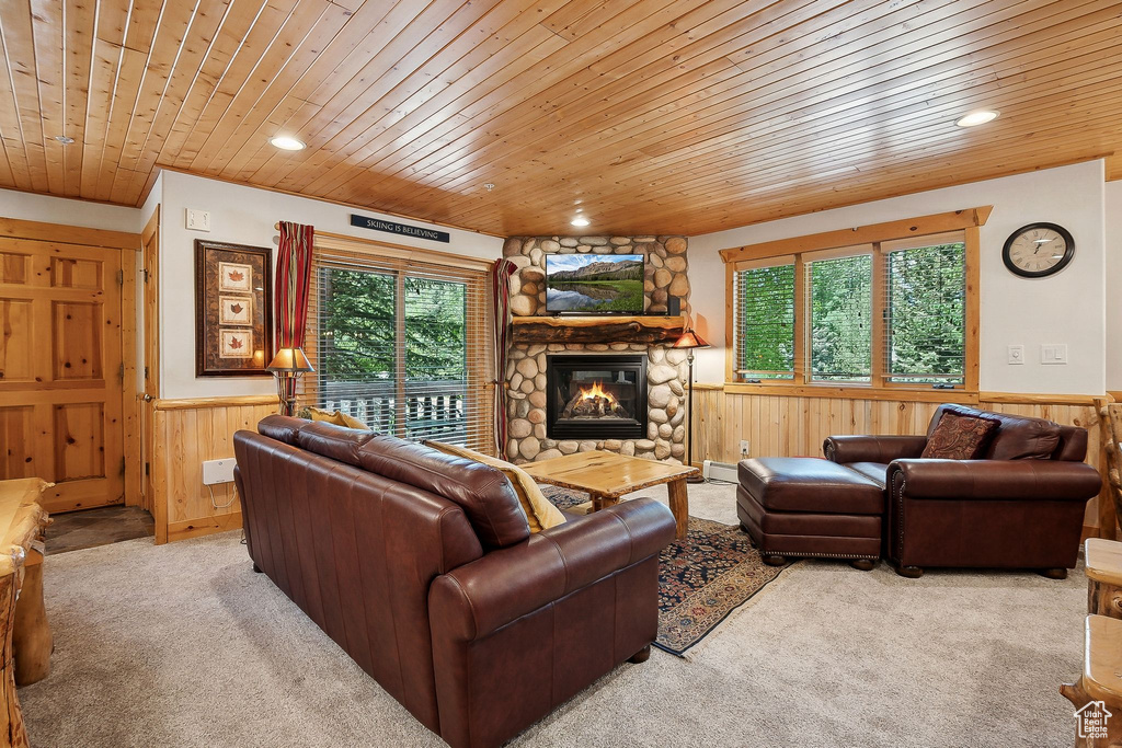 Carpeted living area with wood ceiling, wainscoting, wood walls, a stone fireplace, and recessed lighting
