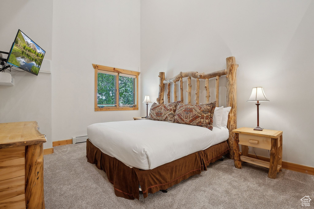 Carpeted bedroom with baseboard heating, baseboards, and a high ceiling