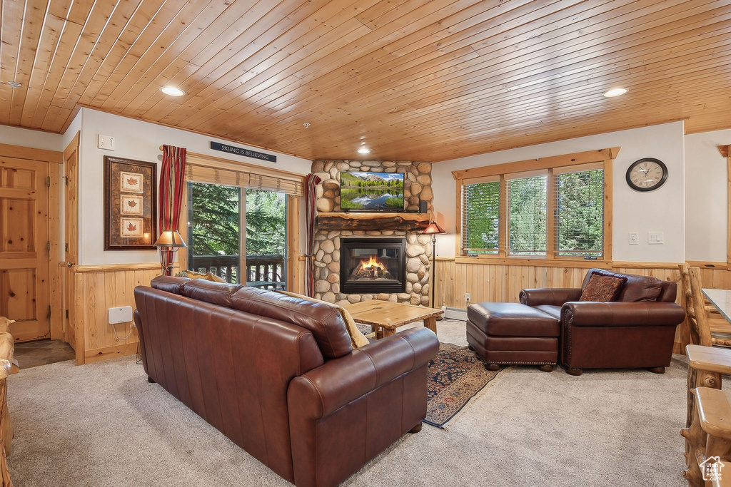 Carpeted living room featuring wainscoting, wood ceiling, wooden walls, a fireplace, and healthy amount of natural light