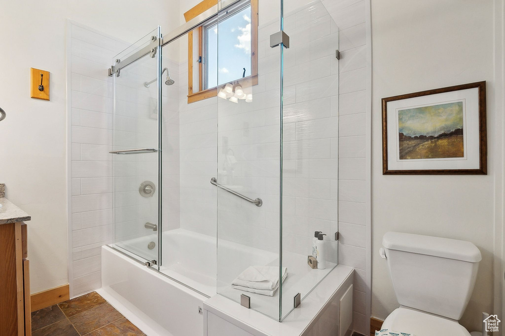 Bathroom with combined bath / shower with glass door, toilet, vanity, baseboards, and stone finish flooring