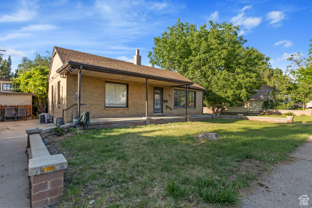 View of front of home featuring central air condition unit, a front yard, a chimney, and brick siding
