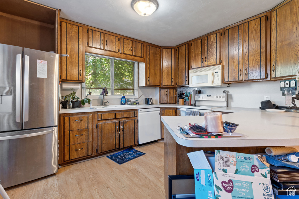 Kitchen featuring white appliances, light countertops, brown cabinets, light wood-style floors, and a sink