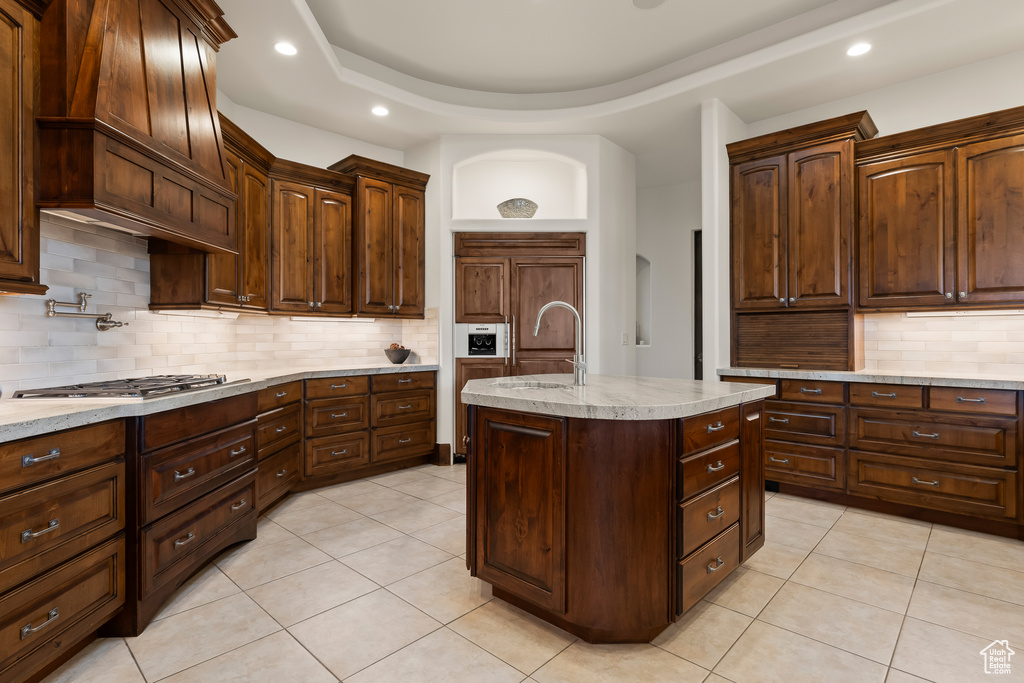 Kitchen featuring stainless steel gas cooktop, light tile patterned floors, backsplash, recessed lighting, and a center island with sink