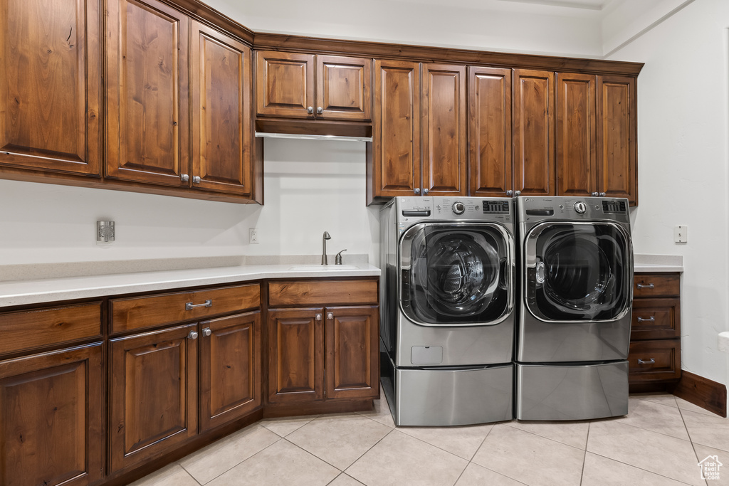Laundry room featuring light tile patterned flooring, cabinet space, washing machine and dryer, and baseboards