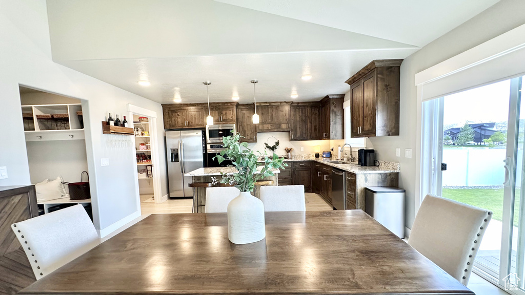 Kitchen with appliances with stainless steel finishes, dark brown cabinets, a sink, a center island, and pendant lighting