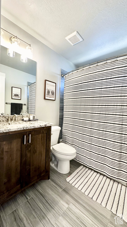 Bathroom featuring toilet, vanity, a textured ceiling, and a shower with curtain