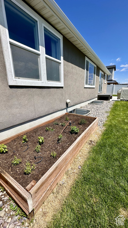 View of side of home featuring stucco siding, a lawn, and a vegetable garden