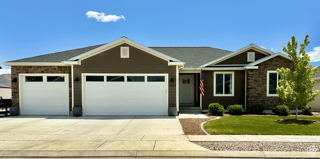 View of front of property with a garage, concrete driveway, a front lawn, and a shingled roof