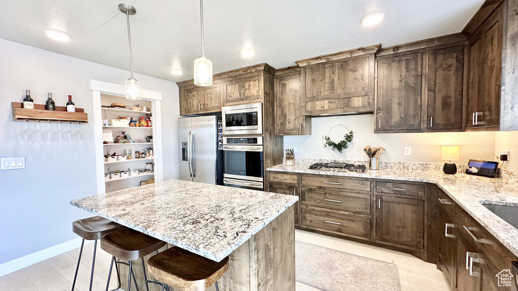 Kitchen featuring appliances with stainless steel finishes, light stone counters, a breakfast bar, and dark brown cabinets